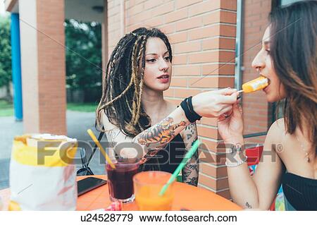 Stock Photo - Girlfriends sharing ice cream at cafe. Fotosearch