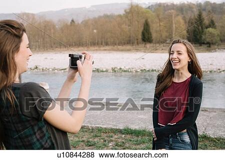 Stock Photo - Girlfriends taking photograph by river, Belluno, Veneto, Italy. Fotosearch