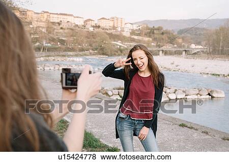 Stock Photo - Girlfriends taking photograph by river, Belluno, Veneto, Italy. Fotosearch
