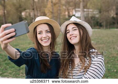 Stock Image - Girlfriends taking selfie in park. Fotosearch