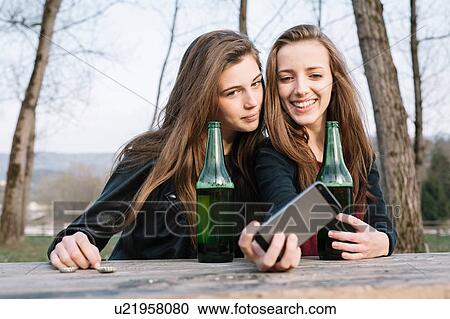 Stock Image - Girlfriends taking selfie with beer in park. Fotosearch
