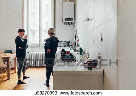 Stock Image - Girlfriends talking in kitchen. Fotosearch