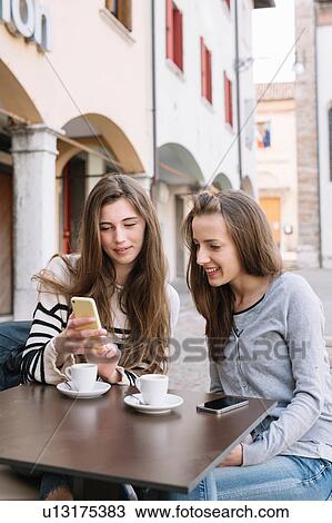Girlfriends using mobile phone at cafe, Belluno, Veneto, Italy View Large Photo Image Stock Image - Girlfriends using mobile phone at cafe, Belluno, Veneto, Italy. Fotosearch