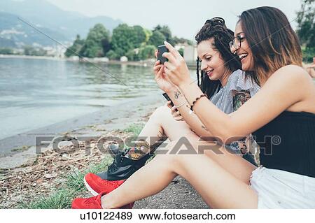 Girlfriends using mobile phone on beach View Large Photo Image Stock Photo - Girlfriends using mobile phone on beach. Fotosearch