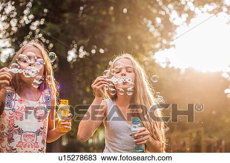 Girls blowing bubbles in park View Large Photo Image Stock Image - Girls blowing bubbles in park. Fotosearch