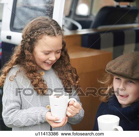 Stock Photograph - Girls drinking hot chocolate beside camper van. Fotosearch