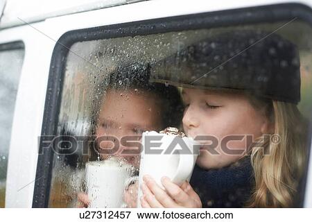 Stock Photo - Girls drinking hot chocolate inside camper van. Fotosearch