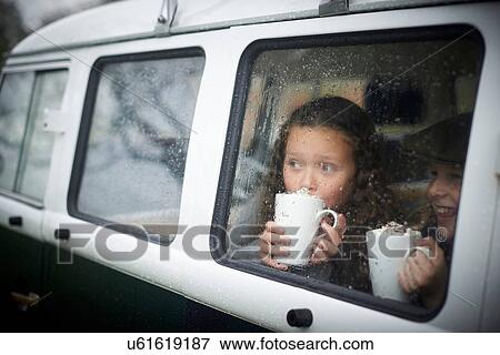 Stock Photo - Girls drinking hot chocolate inside camper van. Fotosearch