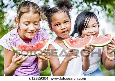 Picture - Girls eating watermelon in park.. Fotosearch
