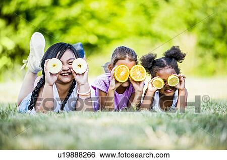 Girls lying side by side in park and covering their eyes with fruit slices, smiling. View Large Photo Image Stock Photograph - Girls lying side by side in park and covering their eyes with fruit slices, smiling.. Fotosearch