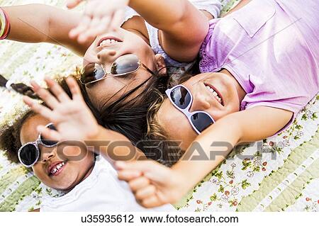 Stock Image - Girls wearing sunglasses and lying on blanket in park.. Fotosearch