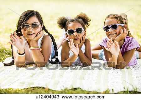 Girls wearing sunglasses and lying side by side on blanket in park, smiling, portrait. View Large Photo Image Stock Image - Girls wearing sunglasses and lying side by side on blanket in park, smiling, portrait.. Fotosearch