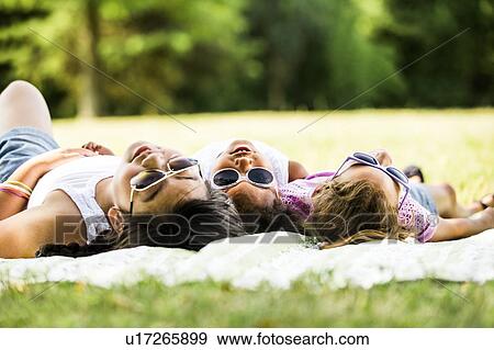 Stock Photo - Girls wearing sunglasses and lying side by side on blanket in park.. Fotosearch