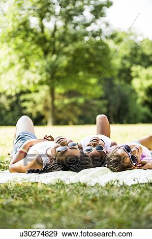 Stock Photo - Girls wearing sunglasses and lying side by side on blanket in park.. Fotosearch