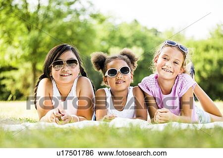 Girls wearing sunglasses and lying side by side on blanket in park, smiling, portrait. View Large Photo Image Stock Photograph - Girls wearing sunglasses and lying side by side on blanket in park, smiling, portrait.. Fotosearch