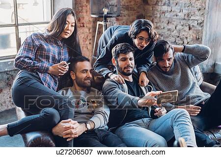 Stock Photo - Group of colleagues on sofa taking selfie. Fotosearch