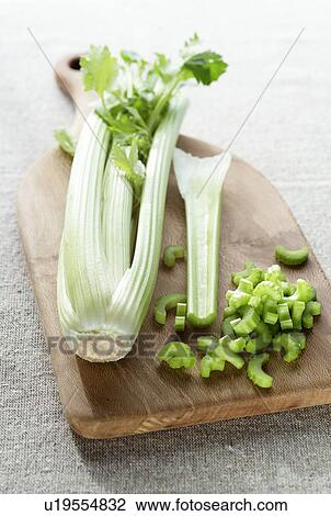 Stock Image - Head of celery on a wooden chopping board with slices of celery lying next to it.. Fotosearch