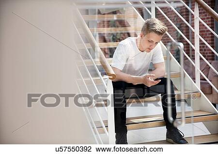 Stock Image - High school boy sitting on school stairway looking at smartphone. Fotosearch