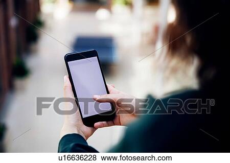 Stock Photo - High school girl in school corridor looking at smartphone, over shoulder view. Fotosearch