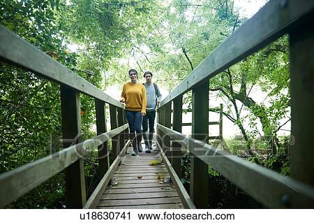 Hiker couple crossing wooden bridge View Large Photo Image Stock Image - Hiker couple crossing wooden bridge. Fotosearch