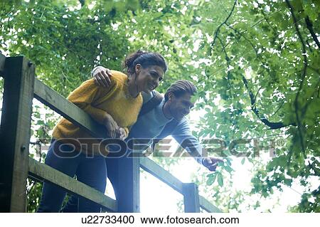 Stock Image - Hiker couple looking over wooden bridge. Fotosearch