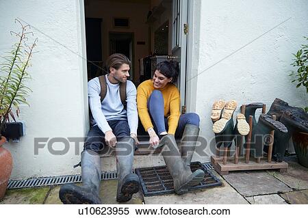 Stock Photography - Hiker couple on doorway putting on wellies. Fotosearch