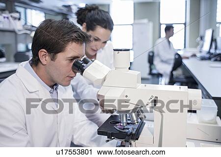 Stock Image - Laboratory assistants using microscope.. Fotosearch