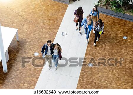 Stock Photo - Male and female university students walking and talking in university lobby, high angle view. Fotosearch