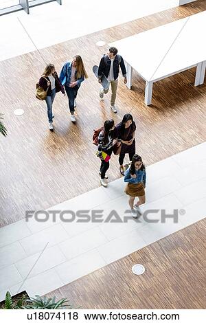Stock Photo - Male and female university students walking and talking in university lobby, high angle view. Fotosearch