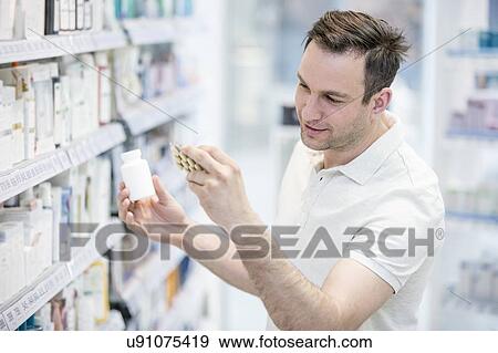 Stock Photo - Male customer reading label on pill blister pack in pharmacy.. Fotosearch