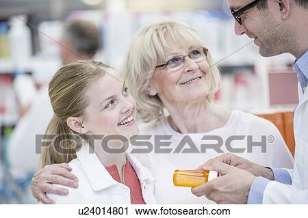 Stock Image - Male pharmacist explaining medication to mature woman and girl in pharmacy.. Fotosearch