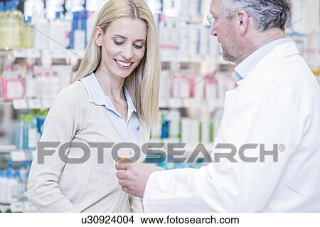 Picture - Male pharmacist giving medicine to woman in pharmacy.. Fotosearch