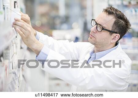 Male pharmacist looking for medicine on shelf in pharmacy. View Large Photo Image Stock Photo - Male pharmacist looking for medicine on shelf in pharmacy.. Fotosearch
