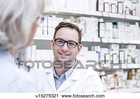 Stock Image - Male pharmacist talking with senior customer in pharmacy.. Fotosearch