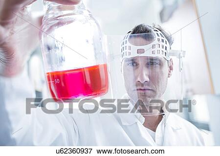 Stock Photo - Male scientist wearing protective mask and holding flask.. Fotosearch