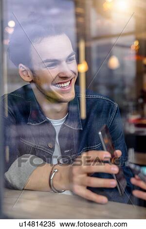 Male student showing smartphone in cafe window seat, view through window View Large Photo Image Stock Photography - Male student showing smartphone in cafe window seat, view through window. Fotosearch