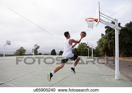 Male teenage basketball player jumping with ball toward basketball hoop View Large Photo Image Stock Image - Male teenage basketball player jumping with ball toward basketball hoop. Fotosearch