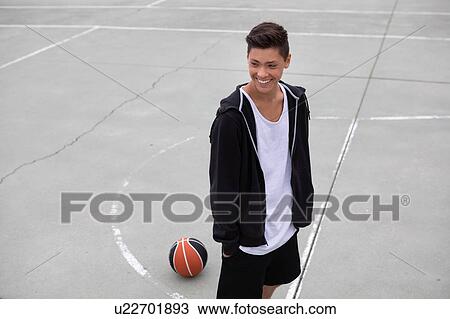 Stock Image - Male teenage basketball player on basketball court, smiling. Fotosearch