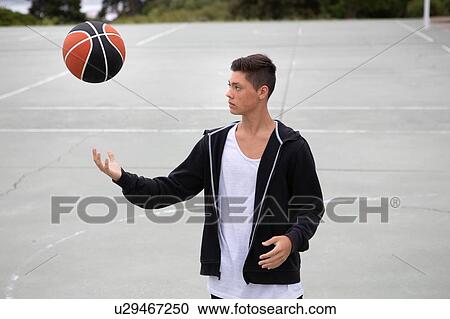 Stock Image - Male teenage basketball player on basketball court throwing and catching ball. Fotosearch
