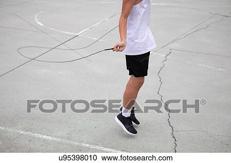 Stock Image - Male teenage basketball player on basketball court skipping, neck down. Fotosearch