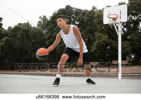 Stock Photo - Male teenage basketball player playing basketball on court. Fotosearch