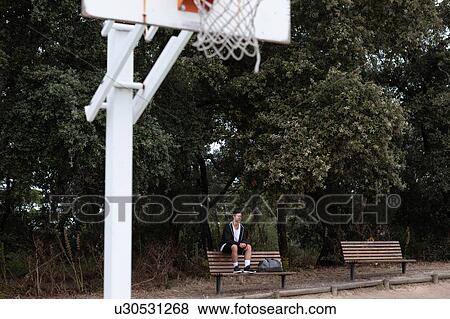 Stock Photo - Male teenage basketball player sitting on park bench by basketball court. Fotosearch