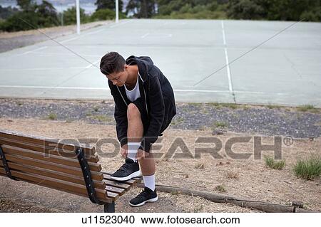 Stock Image - Male teenage basketball player fastening trainers by basketball court. Fotosearch
