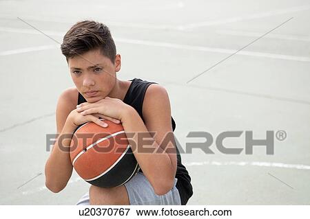 Male teenage basketball player crouching with ball on basketball court, portrait View Large Photo Image Stock Photo - Male teenage basketball player crouching with ball on basketball court, portrait. Fotosearch