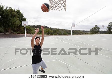 Stock Image - Male teenage basketball player throwing ball toward basketball hoop. Fotosearch
