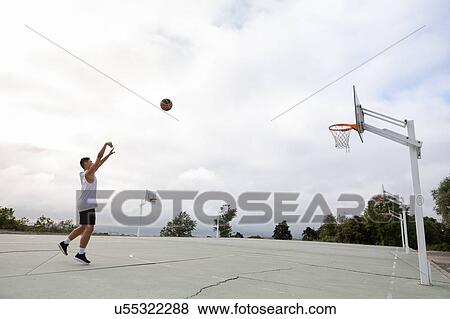 Stock Photo - Male teenage basketball player throwing ball toward basketball hoop. Fotosearch
