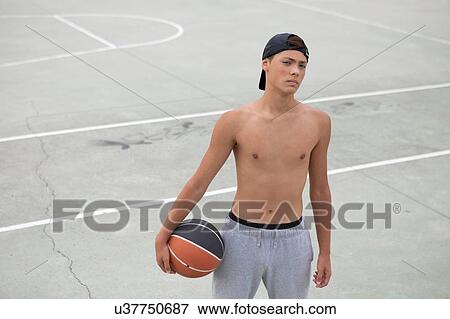 Stock Photo - Male teenage basketball player with ball on basketball court, portrait. Fotosearch