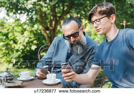 Man and son using cellphone over coffee in garden View Large Photo Image Stock Photo - Man and son using cellphone over coffee in garden. Fotosearch