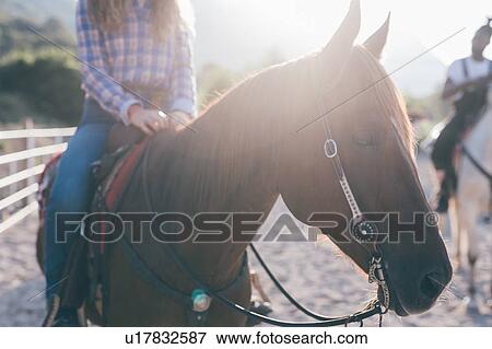 Stock Photo - Man and woman on horseback in rural equestrian arena, cropped. Fotosearch
