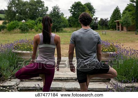 Picture - Man and woman practicing yoga in garden, rear view of tree pose. Fotosearch